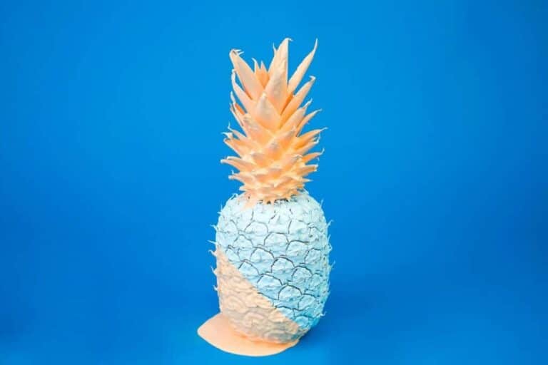 Fruchtige Ananas aus Papier in Pastellfarben vor blauem Hintergrund.