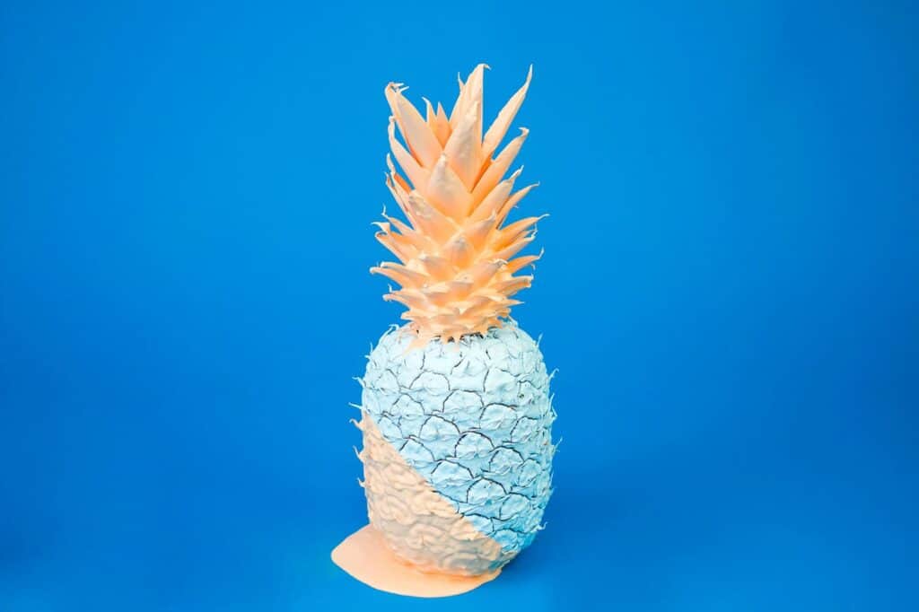 Fruchtige Ananas aus Papier in Pastellfarben vor blauem Hintergrund.