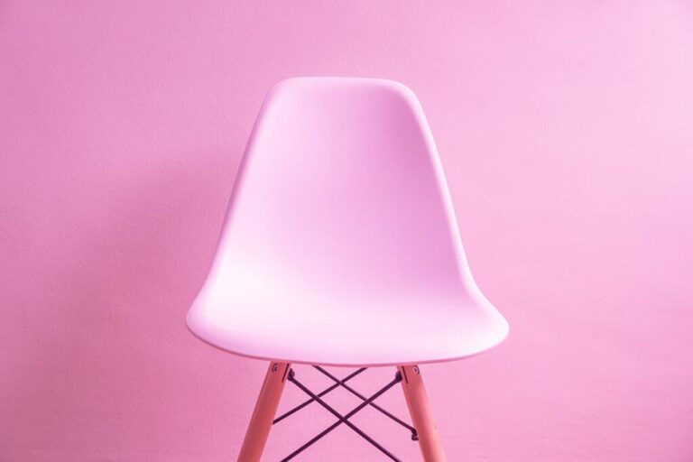 Moderner, weißer Stuhl vor pinkem Hintergrund, minimalistisch gestaltet.