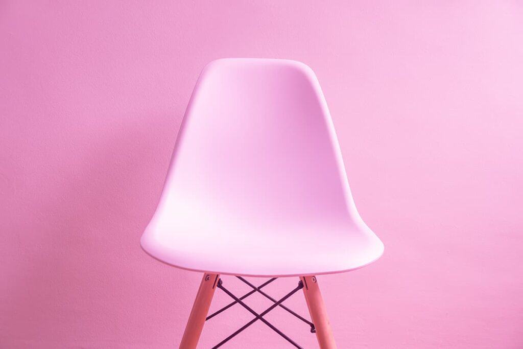 Moderner, weißer Stuhl vor pinkem Hintergrund, minimalistisch gestaltet.